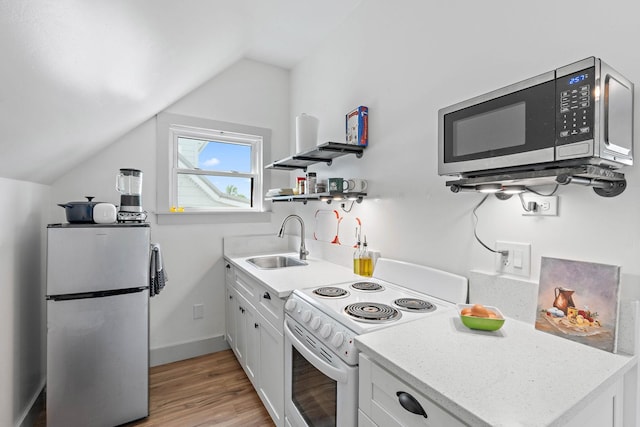 kitchen featuring white cabinets, a sink, light wood finished floors, vaulted ceiling, and stainless steel appliances