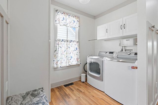 clothes washing area featuring visible vents, baseboards, light wood-type flooring, washing machine and clothes dryer, and cabinet space