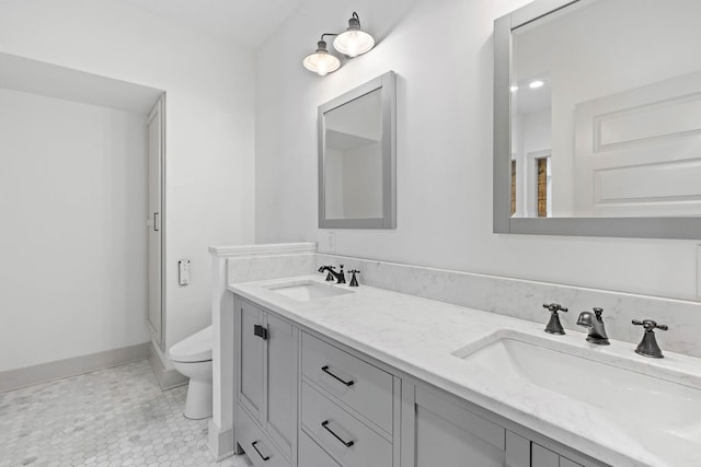 full bathroom featuring double vanity, toilet, baseboards, and a sink