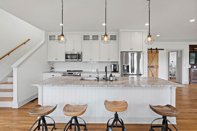 kitchen featuring appliances with stainless steel finishes, a sink, a kitchen island with sink, decorative backsplash, and wood finished floors