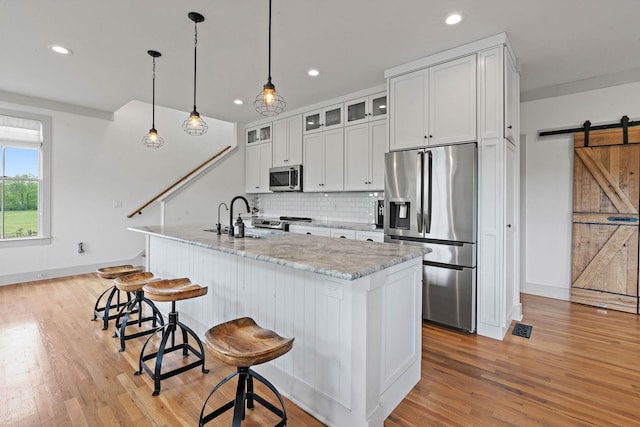 kitchen with a barn door, light wood finished floors, stainless steel appliances, recessed lighting, and tasteful backsplash