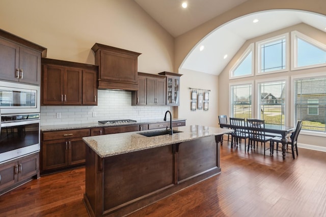 kitchen with backsplash, a sink, dark wood-type flooring, light stone countertops, and appliances with stainless steel finishes