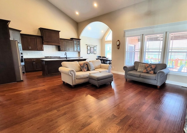 living area with arched walkways, dark wood finished floors, a healthy amount of sunlight, and high vaulted ceiling