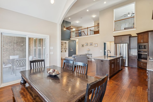dining room featuring arched walkways, a ceiling fan, high vaulted ceiling, and dark wood-style flooring