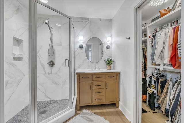 bathroom featuring wood finished floors, a spacious closet, vanity, and a marble finish shower
