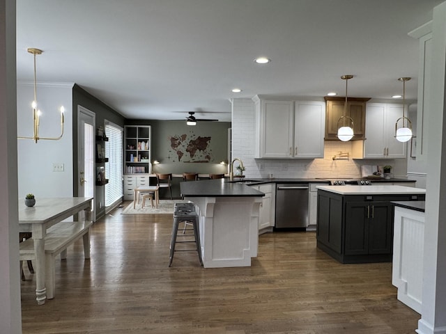 kitchen with a peninsula, stainless steel dishwasher, a sink, dark countertops, and decorative backsplash