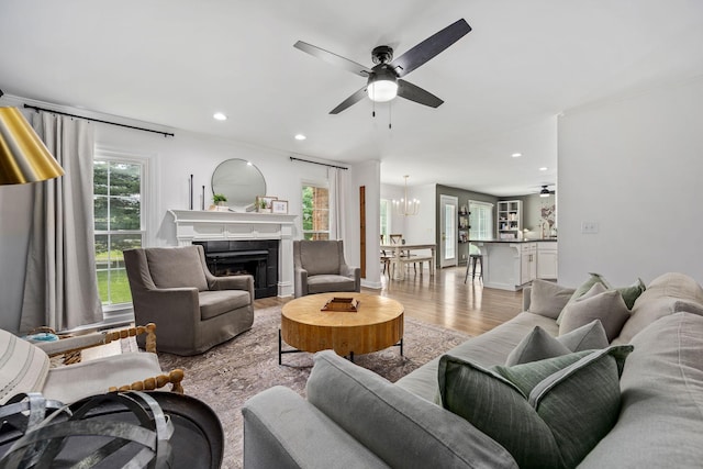 living room featuring ceiling fan with notable chandelier, a fireplace, light wood-style flooring, and plenty of natural light
