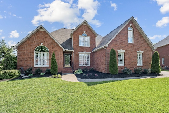 traditional home featuring brick siding, a shingled roof, and a front yard