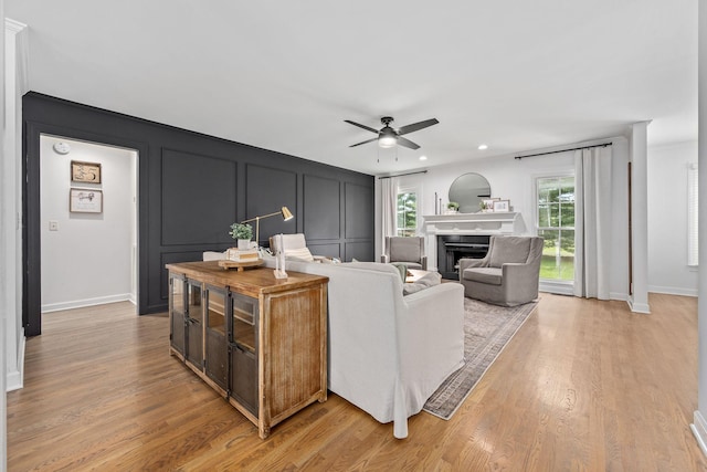 living area featuring a ceiling fan, light wood-style floors, a fireplace, and a decorative wall