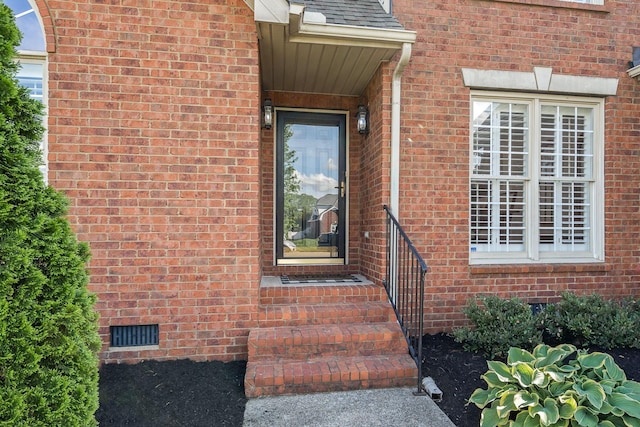 view of exterior entry with visible vents, crawl space, and brick siding