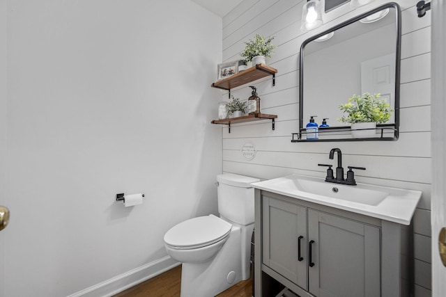 bathroom featuring wood walls, wood finished floors, toilet, and vanity