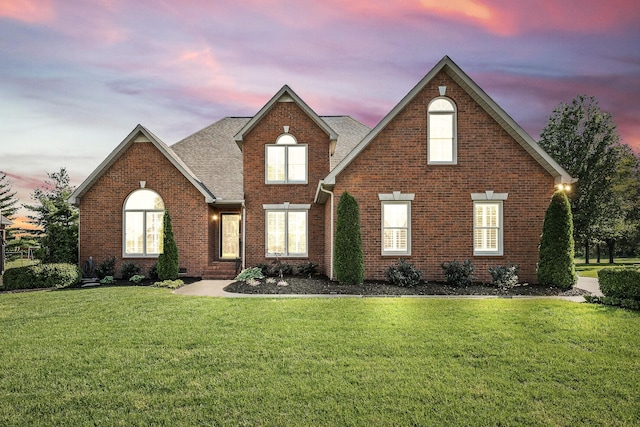 traditional-style home featuring a front lawn, roof with shingles, and brick siding