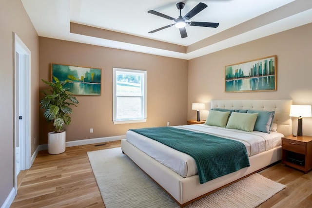 bedroom featuring baseboards, a ceiling fan, a tray ceiling, and light wood-style floors