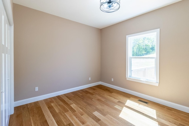 spare room with a chandelier, light wood-style floors, visible vents, and baseboards