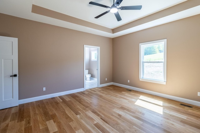 empty room with light wood finished floors, a tray ceiling, visible vents, baseboards, and ceiling fan