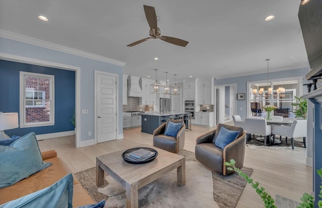 living room featuring a wealth of natural light, crown molding, light wood finished floors, and ceiling fan with notable chandelier