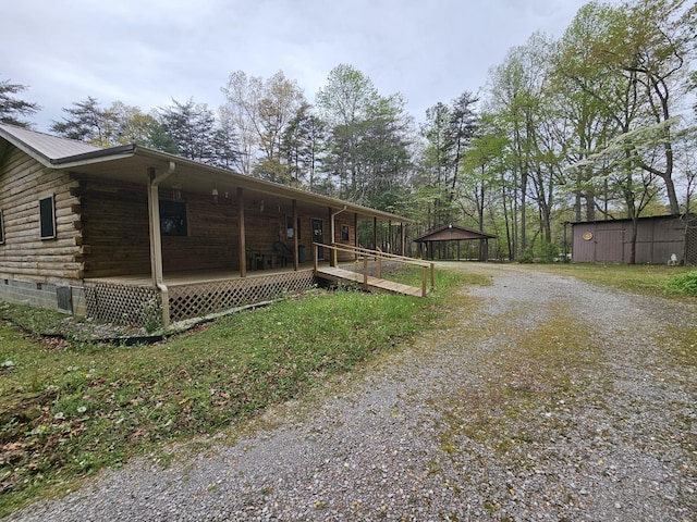 view of property exterior featuring gravel driveway, covered porch, and log siding