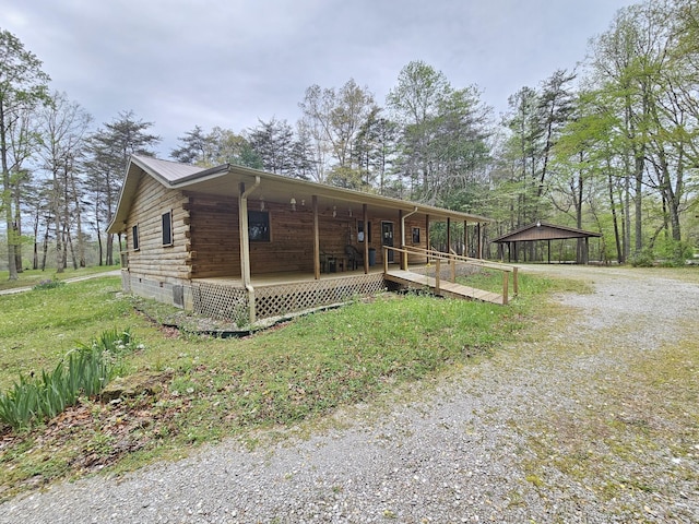 view of front of house with gravel driveway, log exterior, and a porch