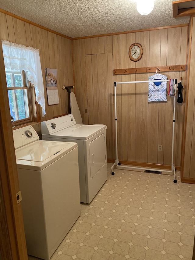 laundry room featuring a textured ceiling, washer and clothes dryer, wood walls, and laundry area