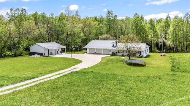 back of property featuring a garage, a yard, a trampoline, and a view of trees