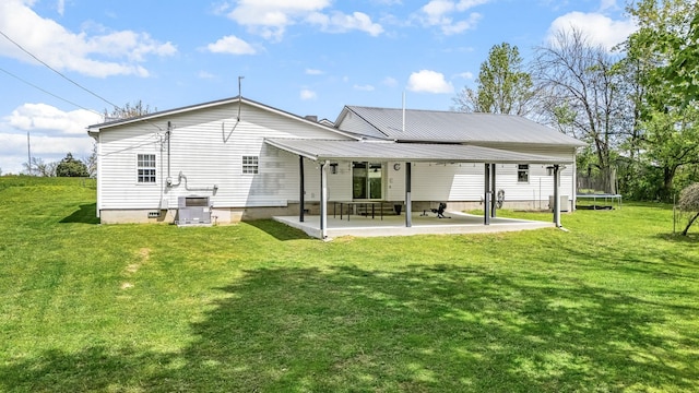 back of property featuring a patio area, a lawn, metal roof, and a trampoline