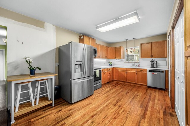 kitchen with light countertops, a sink, decorative light fixtures, light wood-style flooring, and appliances with stainless steel finishes
