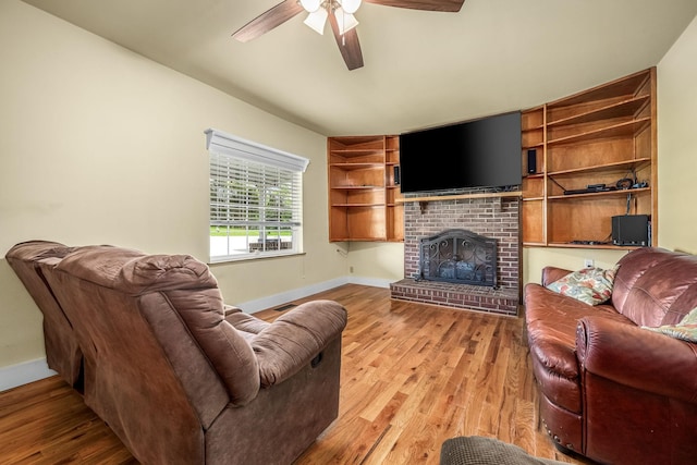 living room with ceiling fan, baseboards, a brick fireplace, and wood finished floors