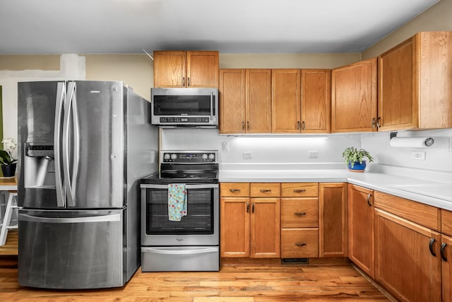 kitchen featuring light wood finished floors, stainless steel appliances, light countertops, and brown cabinets