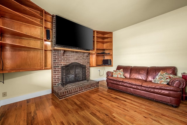 living room featuring baseboards, wood finished floors, a fireplace, and built in features