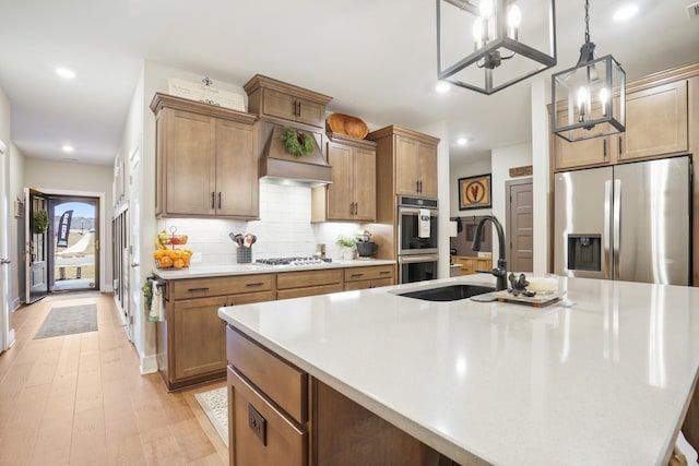 kitchen featuring an island with sink, light countertops, a sink, a chandelier, and appliances with stainless steel finishes