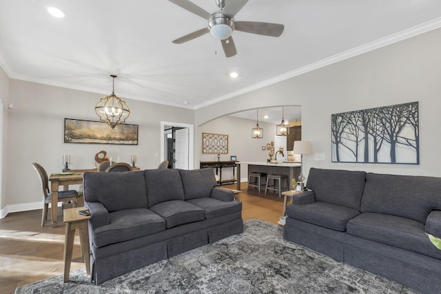 living area featuring wood finished floors, ceiling fan with notable chandelier, arched walkways, baseboards, and ornamental molding