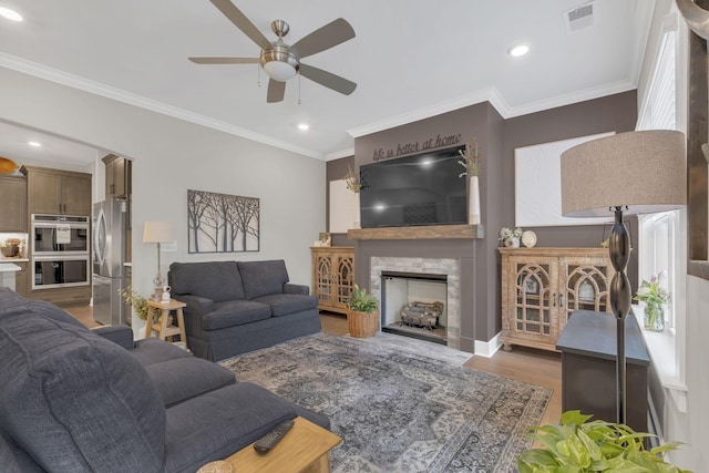 living room with visible vents, wood finished floors, ceiling fan, a fireplace, and ornamental molding