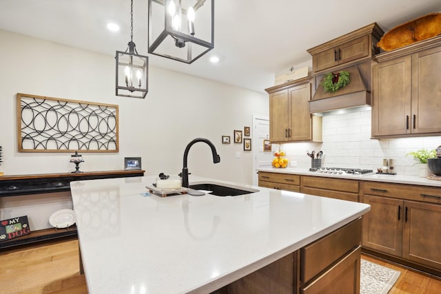 kitchen featuring light wood finished floors, a sink, decorative backsplash, light countertops, and an island with sink