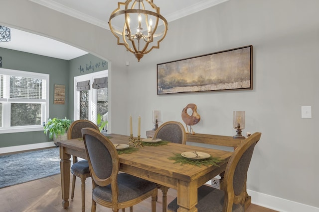 dining space with arched walkways, baseboards, an inviting chandelier, wood finished floors, and crown molding