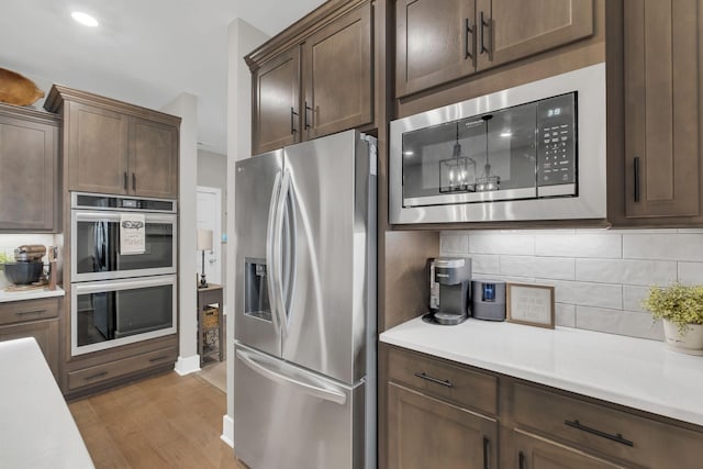 kitchen with light countertops, light wood finished floors, tasteful backsplash, and appliances with stainless steel finishes