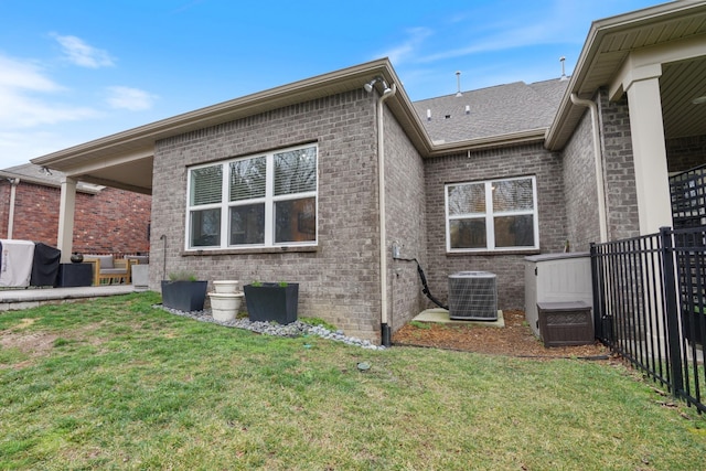 rear view of house with brick siding, central air condition unit, a lawn, and fence