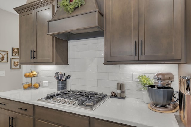 kitchen featuring stainless steel gas stovetop, light countertops, custom range hood, and tasteful backsplash