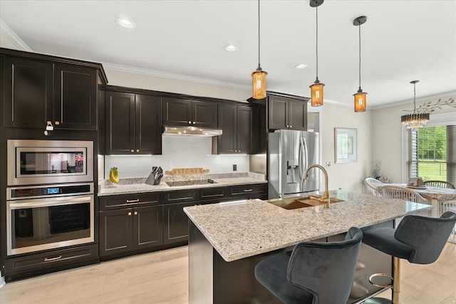 kitchen featuring light stone countertops, stainless steel appliances, a sink, and crown molding