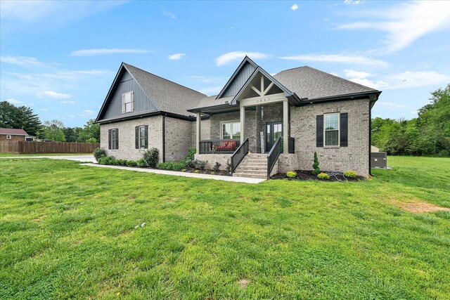 craftsman house featuring a porch, fence, brick siding, a shingled roof, and a front yard