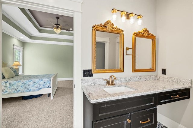 ensuite bathroom with a raised ceiling, vanity, crown molding, baseboards, and ceiling fan