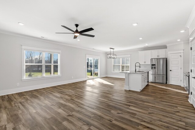 unfurnished living room with ceiling fan with notable chandelier, a healthy amount of sunlight, a sink, and crown molding