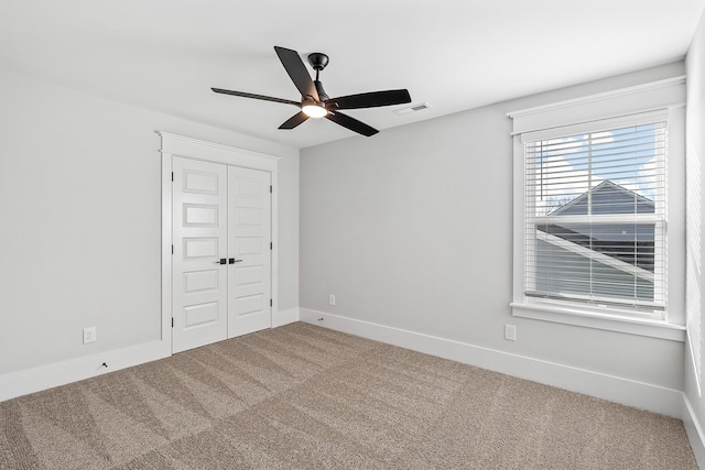 carpeted spare room with baseboards, visible vents, and ceiling fan