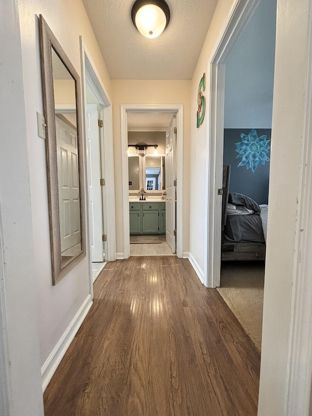 corridor with baseboards, dark wood-style floors, a textured ceiling, and a sink