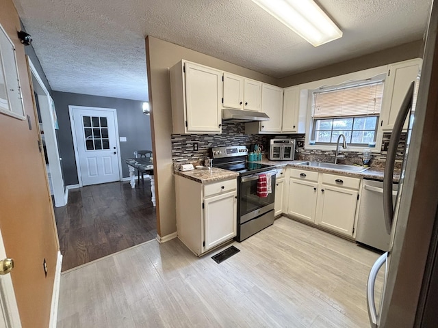 kitchen with a sink, light wood-style floors, stainless steel appliances, under cabinet range hood, and visible vents