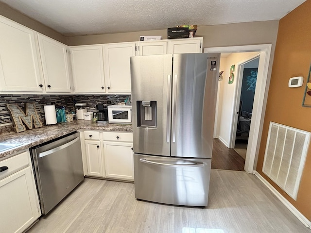 kitchen with stainless steel appliances, tasteful backsplash, light wood-type flooring, visible vents, and white cabinetry