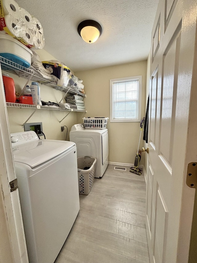 clothes washing area featuring a textured ceiling, laundry area, light wood finished floors, washing machine and dryer, and visible vents