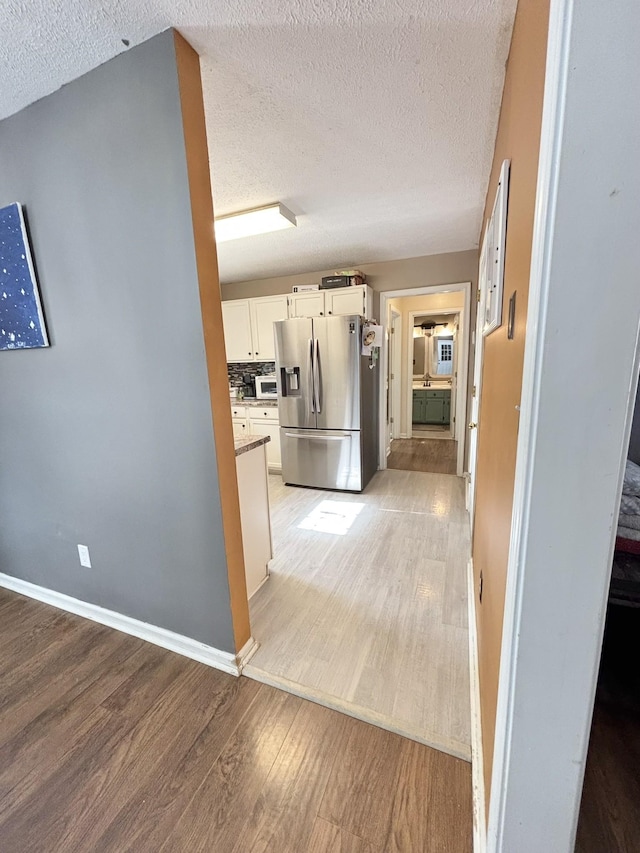 hallway with light wood-style floors, a textured ceiling, and baseboards