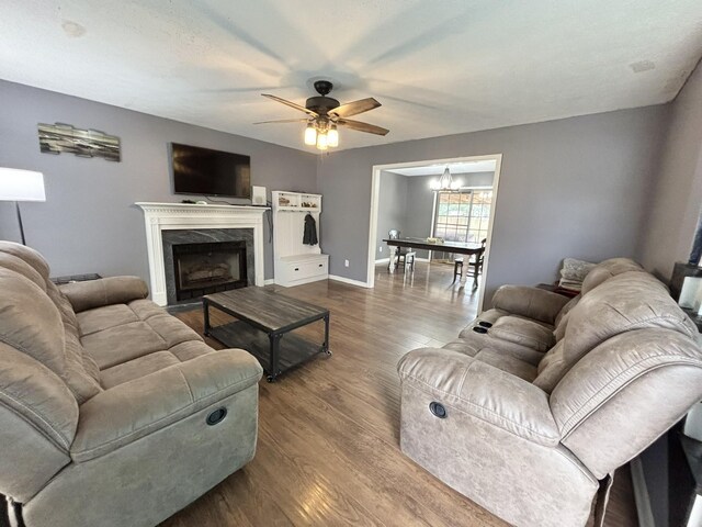 living room featuring ceiling fan with notable chandelier, baseboards, a fireplace, and dark wood-style flooring
