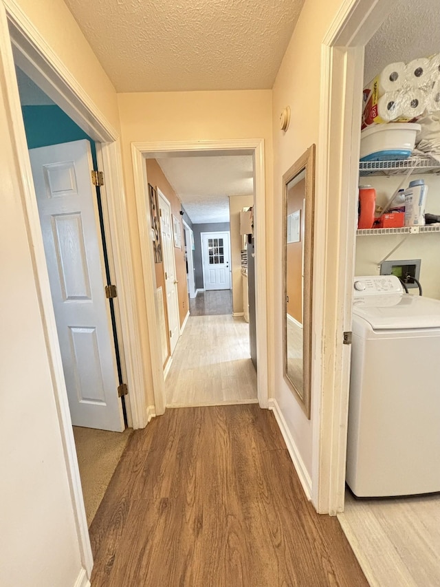 corridor with baseboards, wood finished floors, a textured ceiling, and washer / clothes dryer