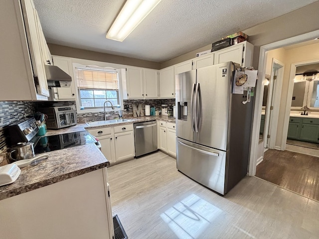 kitchen featuring light wood-style flooring, a textured ceiling, a sink, backsplash, and appliances with stainless steel finishes